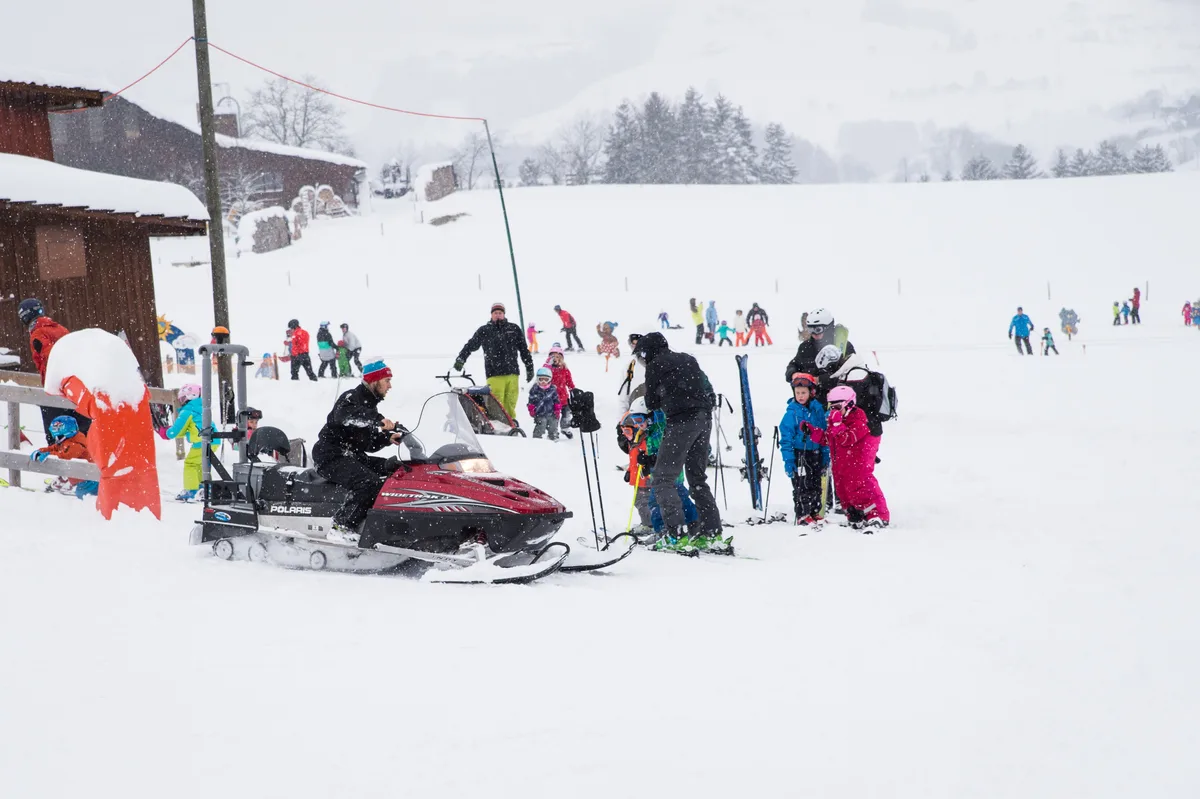 Ein Schneetöff und Kinder auf Ski auf einer Alp. 